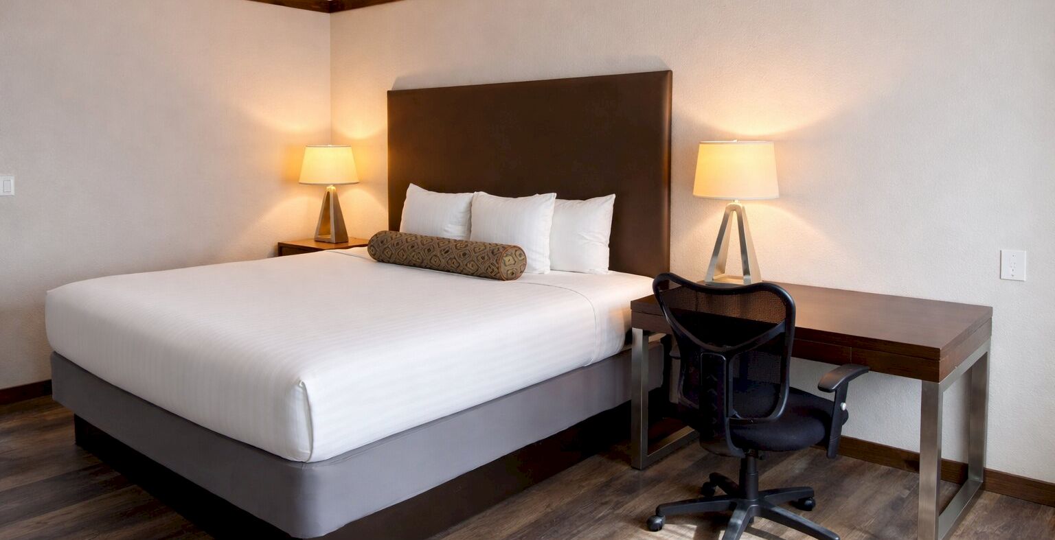 A tidy hotel bedroom with a large bed, two lamps, a desk, and a chair.