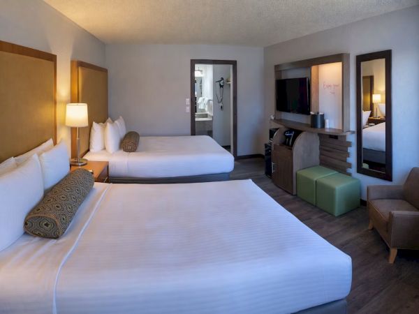 A modern hotel room with two neatly made beds, bedside lamps, and a TV by the mirror.
