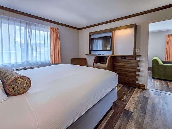 A cozy bedroom with a large bed, window curtains, wood floors, and a built-in wall unit/fireplace area.