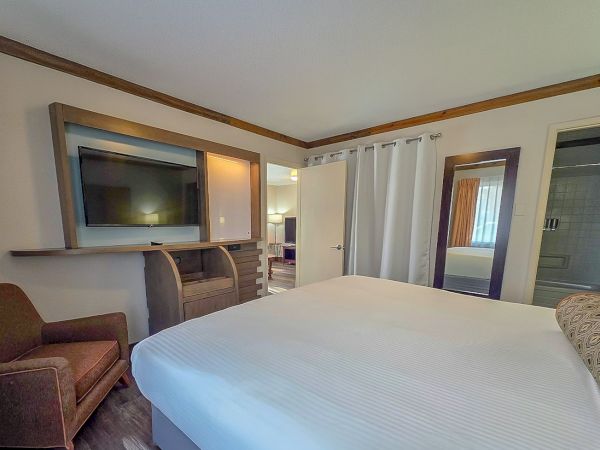 A modern hotel-style bedroom with a large bed, TV, curtains, and mirrors reflecting an adjacent sitting area.