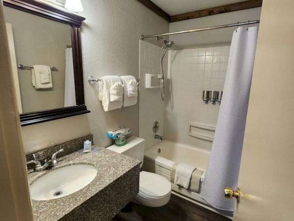A cozy bathroom with a granite vanity, mirror, toilet, bathtub with showerhead, and fresh white towels.