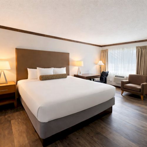 A neatly made hotel bedroom with a large bed, bedside tables, lamps, and a window with curtains.
