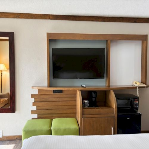 A motel room TV mounted in a wooden cabinet beside a mini kitchen with microwave and coffee maker.