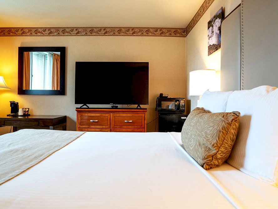A cozy hotel room with two white beds, a wall-mounted TV on a wooden dresser, and bedside lamps.