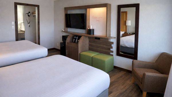 A hotel room with two beds, a TV console, mirrors, and a small desk chair.