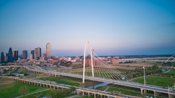 Aerial view of a city skyline with a cable-stayed bridge spanning a river under a blue sunset sky.
