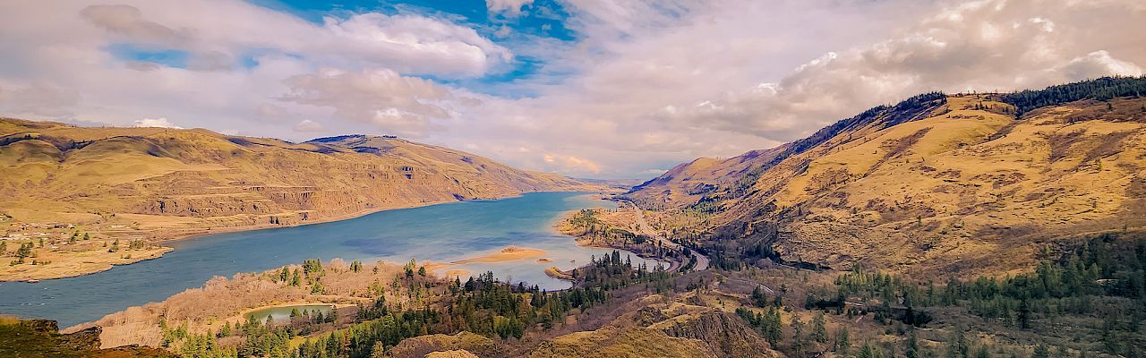 A sweeping view of a winding river through golden hills under dramatic clouds.
