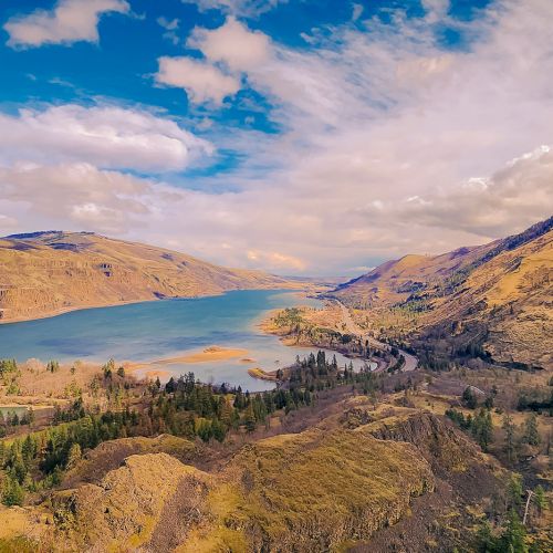 A sweeping view of a winding river through golden hills under dramatic clouds.